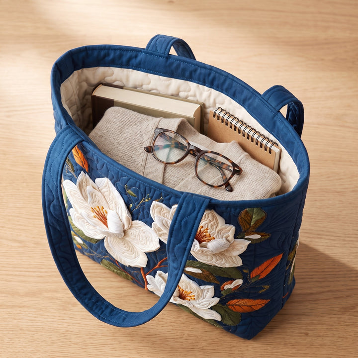 Bolso Artesanal Acolchado — Magnolia Delicada: con un libro de tapa dura, un suéter doblado y lentes de lectura